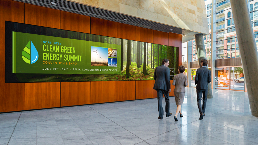 People walking past a large video wall in a lobby. The wall says “Clean Green Energy Summit.