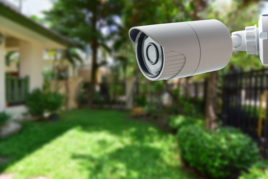 A smart security camera installed outside with a green yard in the background.