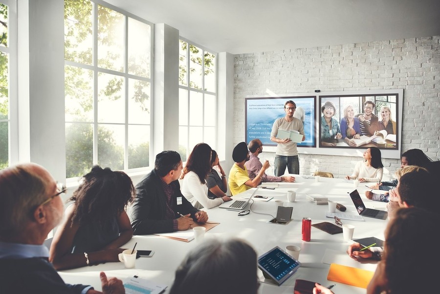 A busy conference room featuring two HD monitors.