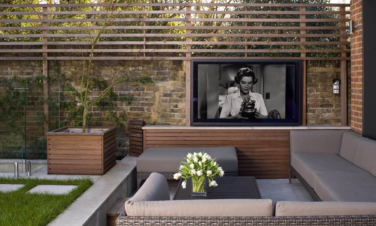 an outdoor patio area with an old-time movie playing on an outdoor tv. Wooden furniture