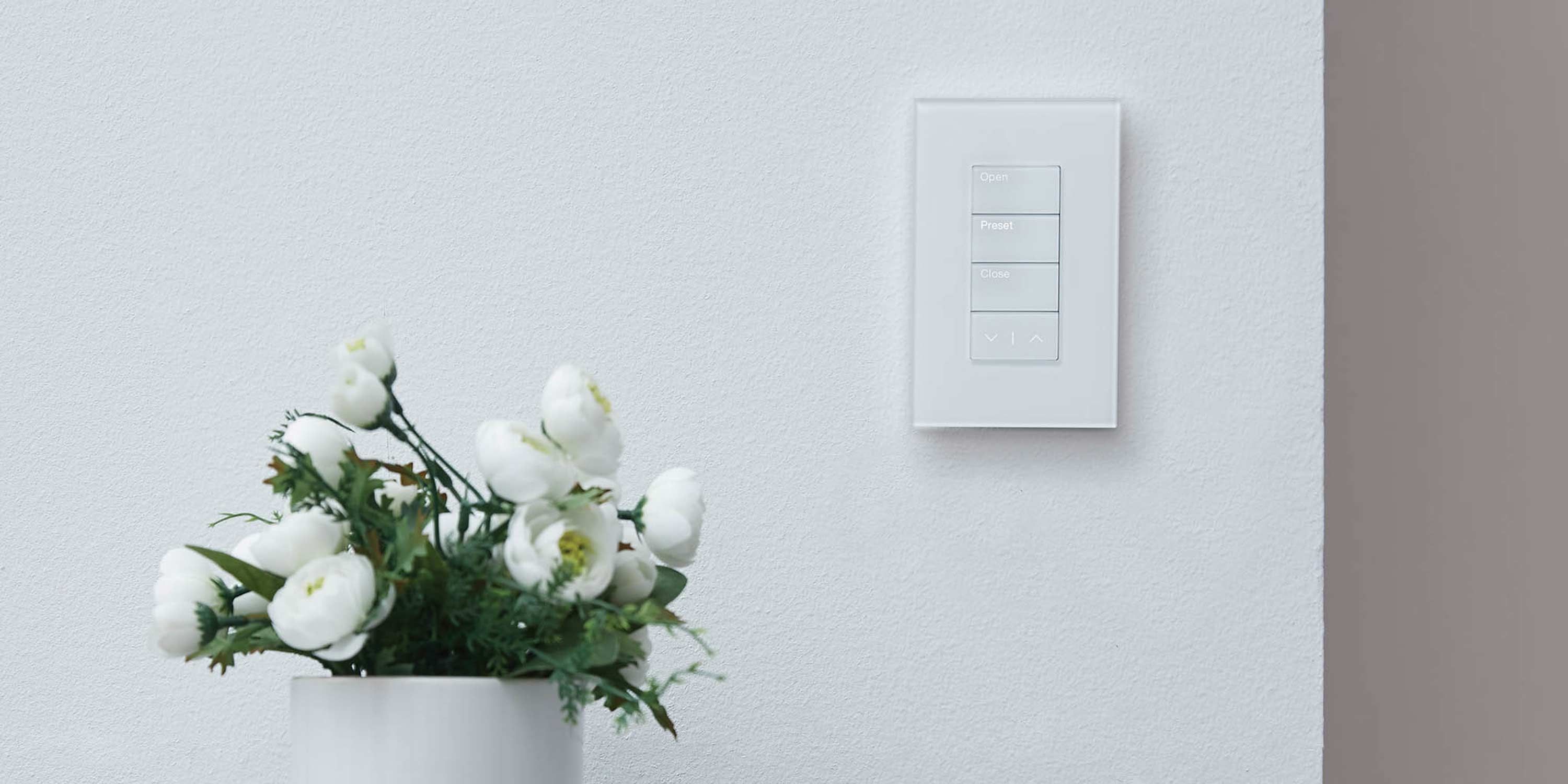 White lutron keypad on a white wall next to a vase of flowers