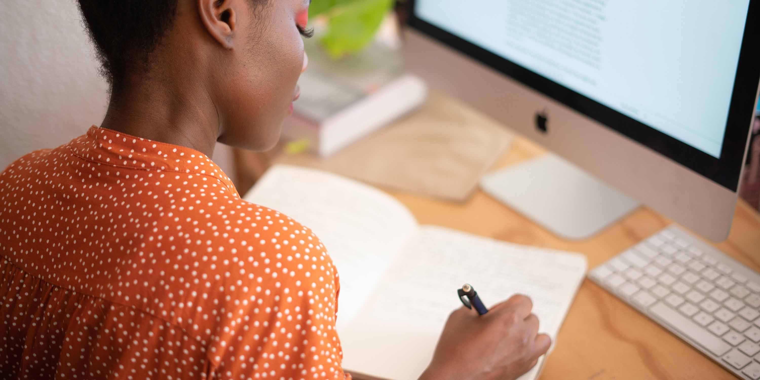 woman sitting in front of a macbook writing in a journal