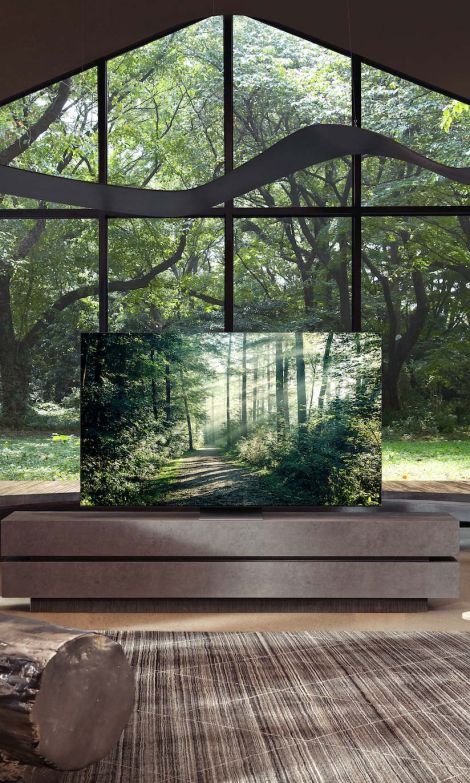 A samsung TV with a forest scene in front of large windows