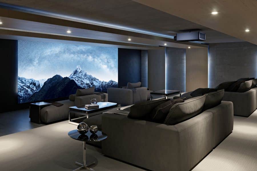 A large home movie theater with chaise lounges, a Sony projector, and a movie screen depicting snow-capped mountains.
