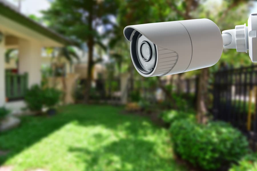 A smart security camera installed outside with a green yard in the background. 