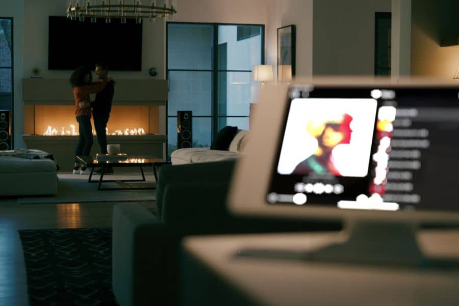 Couple dancing in the background by their living room fireplace with a home audio control pad at the forefront of the photo.