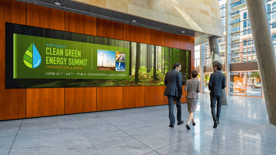People walking past a large video wall in a lobby. The wall says “Clean Green Energy Summit.”